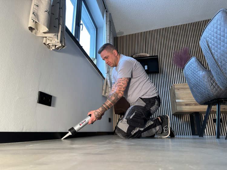 Konzentrierter Handwerker mit Tattoos verfugt in grauem Shirt den Boden