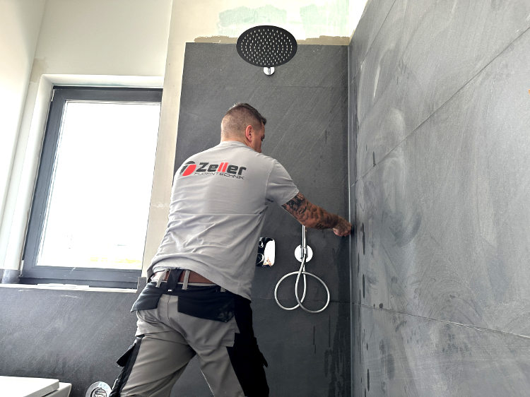 Ein Handwerker mit Zeller Shirt montiert eine Regendusche im grauen Bad