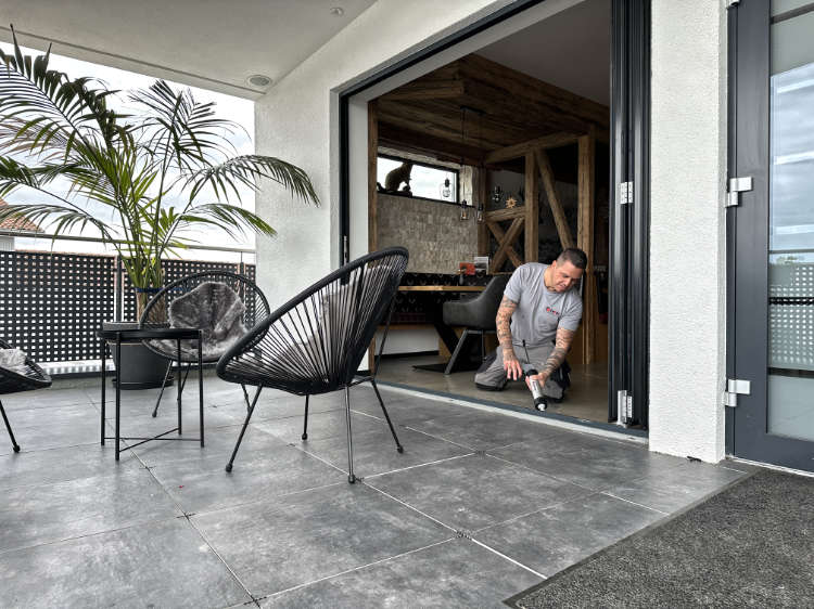 Ein taetowierter Mann arbeitet konzentriert an einer Terrassentuer aus Glas