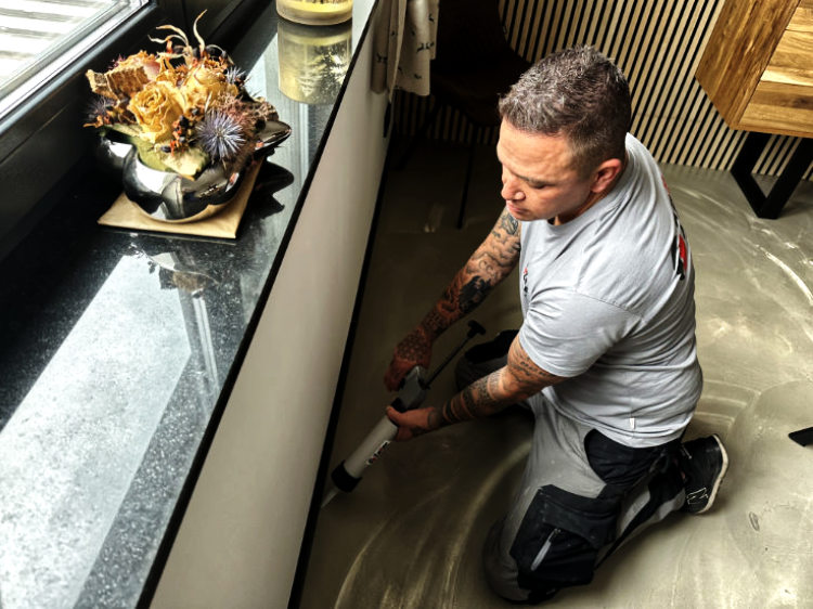 Ein konzentrierter Handwerker mit Tattoos verfugt kniend eine Fensterbank